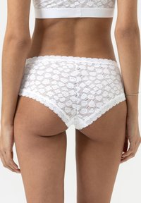 Witte kanten slip met bloemenpatroon, gegolfde randen en een zachte textuur. Elastische tailleband zichtbaar, wat zorgt voor een goede pasvorm.