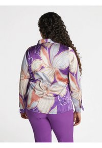 Blusa a maniche lunghe in tessuto setoso, con sfondo viola e grandi motivi floreali in crema, arancione e lavanda. Fit slim con polsini.