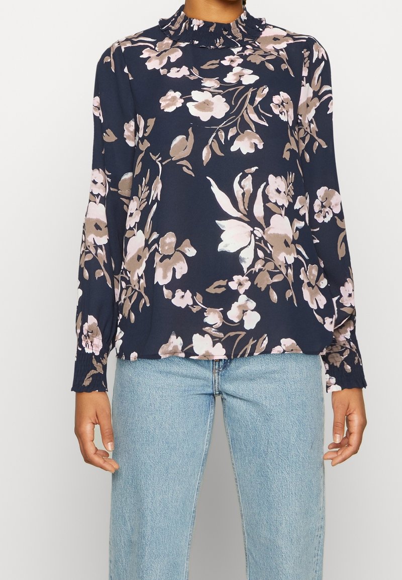 Blusa blu navy con motivo floreale in rosa chiaro e beige, con colletto arricciato e maniche lunghe con polsini elasticizzati. Tessuto morbido e leggero.