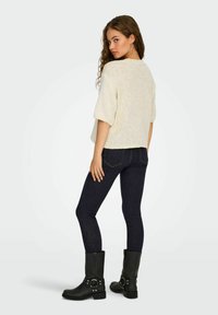 Chunky strikket creme trøje med korte ærmer, parret med mørkeblå skinny jeans og sorte knæhøje støvler med ankelremme og nitter.