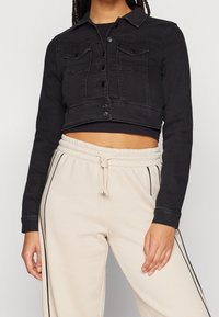 Černá zkrácená džínová bunda s knoflíkovým zapínáním, dvěma předními kapsami a klasickým límečkem. Má dlouhé rukávy a přiléhavý střih.