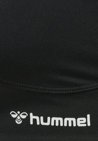 Svart idrottstopp med ribbad textur. Har en framträdande vit logotyp "hummel" och en bi-emblem. Designad för aktiv träning.