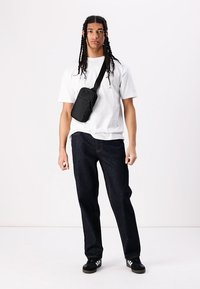 Svart midjeveske, hvit t-skjorte og mørkeblå jeans. Uformell antrekk med rette denim-fit og sorte joggesko med tre hvite striper.