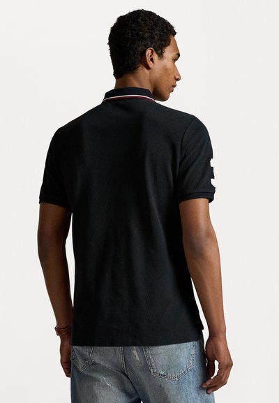 Cămașă polo neagră cu un accent alb pe mânecă și tiv roșu la guler, asortată cu blugi deschiși la culoare, ușor distruși. Design minimalist.
