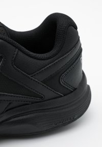 Chaussure de sport noire avec une tige en cuir texturé, un col rembourré et une semelle en caoutchouc durable dotée d'une bande de roulement prononcée pour une meilleure traction.