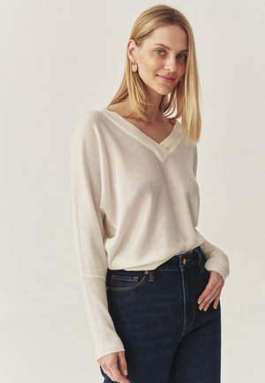 Creme V-hals, lange mouwen pullover trui, gemaakt van zachte stof met geribbelde manchetten, gecombineerd met donker gewassen high-waisted jeans.