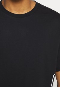 Czarny bawełniany t-shirt z okrągłym dekoltem, krótkimi rękawami i prostym krojem. Zauważalne białe akcenty wzoru na dole.