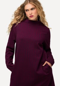 Langärmliges Kleid in Dunkellila mit einem texturierten Hahnentrittmuster. Verfügt über einen hohen Kragen und seitliche Taschen für zusätzlichen Komfort.