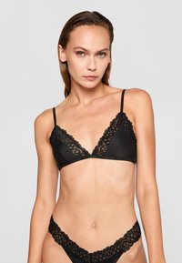Črn bralette z čipkastim robom in ujemajočim se tangicami, ki se ponaša z satenskim videzom, trikotnimi košaricami, nastavljivimi naramnicami in cvetličnimi čipkastimi detajli.