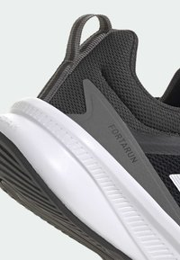 Baskets de sport noires avec une tige en mesh texturé, accents gris et une semelle en caoutchouc blanche avec des nervures. Logo et détail "FORTARUN" visibles.