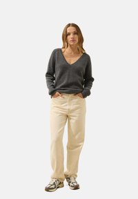 Szary sweter w serek z długimi rękawami, zestawiony z jasnymi kremowymi spodniami i szaro-białymi sneakerami o teksturowanych podeszwach. Prosty design.