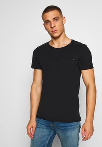 Camiseta negra de manga corta hecha de tela suave, con cuello redondo y un solo bolsillo en el pecho. El diseño es minimalista y ajustado.
