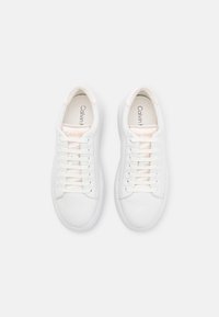 White leather sneakers with a rounded toe, flat laces, and light pink accents on the tongue. Calvin Klein logo printed inside.