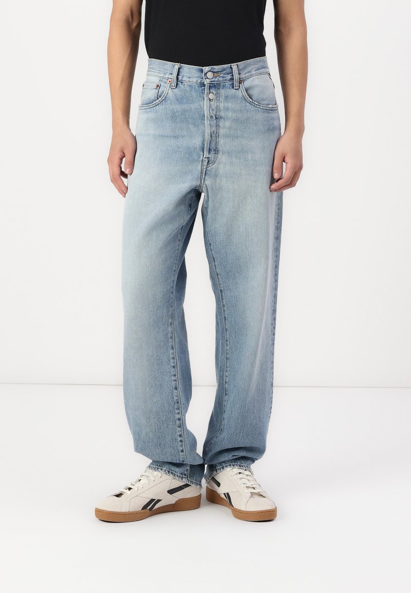 Vaqueros de mezclilla azul claro con un corte holgado, cintura alta, diseño de cinco bolsillos y un ligero desgaste. Combinados con zapatillas blancas con acentos negros.