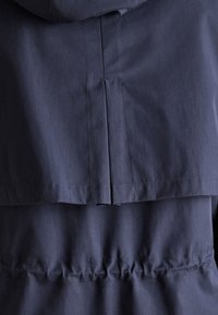 Tessuto blu navy con piega verticale e cucitura orizzontale, che mostra il dettaglio della parte posteriore strutturata del capo.