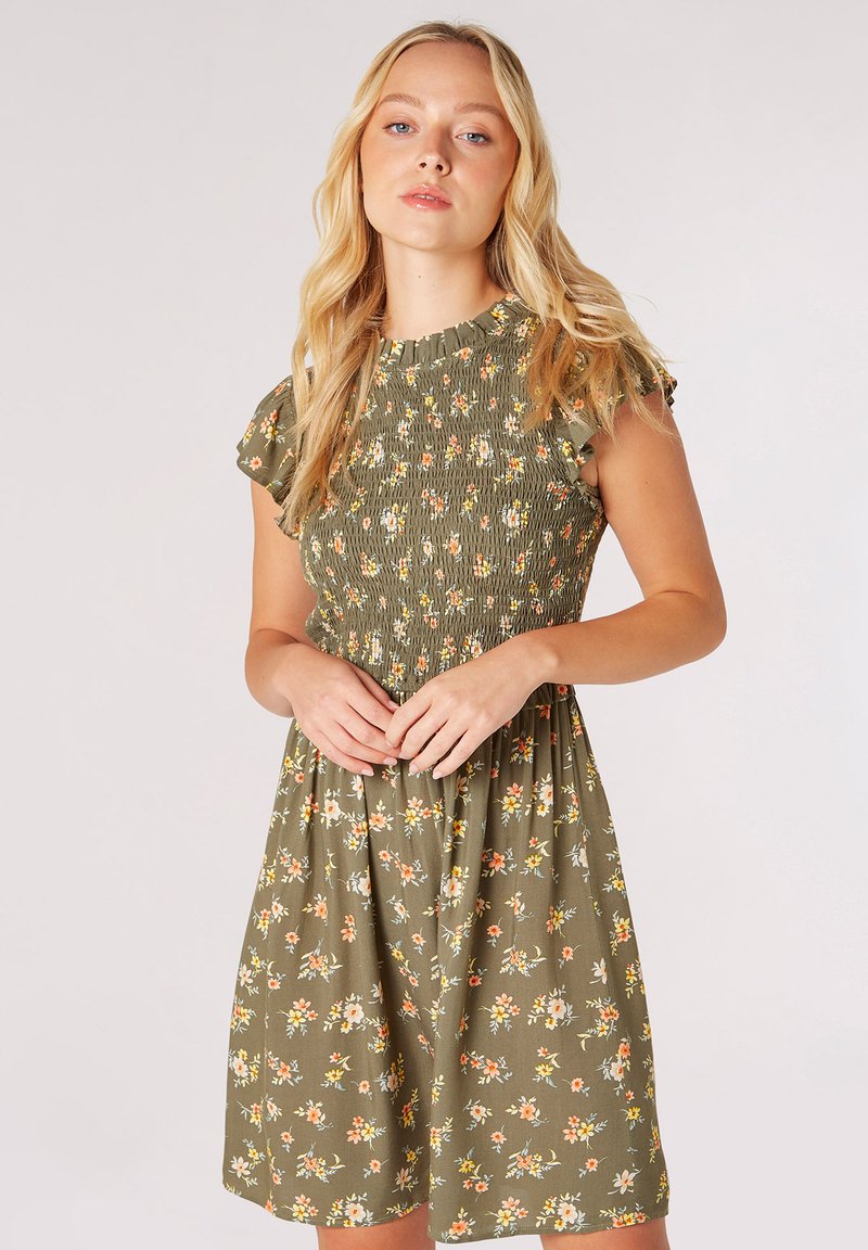 Blomsterklänning i olivgrön med korta volangärmar, smockad bodice och en utsvängd kjol som har flerfärgade blommönster.