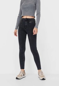 Svarta högmidjade skinny jeans med en slät textur, framfickor och en skräddarsydd passform, tillsammans med en cropped grå långärmad topp.