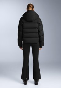 Crni puffer jakna s kapuljačom, koja ima prešani dizajn i skraćeni siluetu. Nosena preko uskih crnih hlača s patentnim zatvaračima na gležnjevima.
