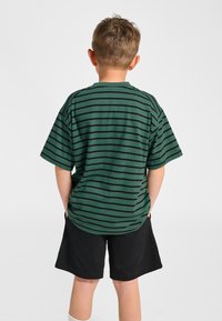 Grön randig t-shirt med svarta horisontella ränder, korta ärmar och en avslappnad passform, matchad med svarta shorts. Bakifrån.