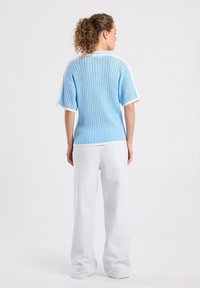 Light blue knitted top with short sleeves, featuring a loose fit and white accents. Paired with light gray wide-leg sweatpants.