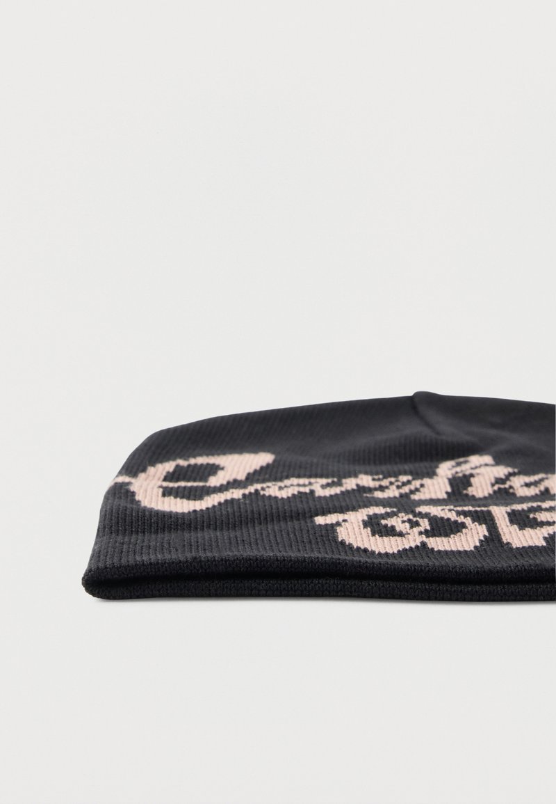 Schwarze Strickmütze mit beigefarbener, kursiver Schrift, teilweise sichtbar, vor schlichtem weißem Hintergrund.