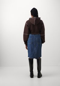 Brun kort hoodie med vit sömnad, i kombination med en blå denimpennkjol och knähöga svarta glänsande stövlar.