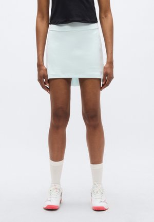Jasnoniebieska sportowa spódnica o dopasowanym kroju, gładkiej fakturze i wykończeniu u dołu. Połączona z białymi trampkami i kremowymi skarpetkami.