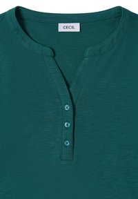Teal tričko s krátkým rukávem a véčkovým výstřihem, s tříknoflíkovou légou, vyrobené z měkkého materiálu s jemným melírovaným vzorem. Značka: CECIL.