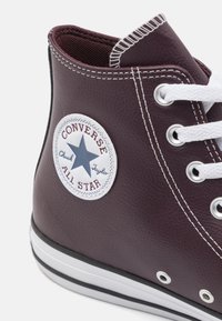 Burgundy högskor med vit gummisula, vita snören och metallöglor. Har en cirkulär logopatch med en blå stjärna.