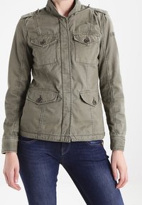 Olivengrøn militærinspireret jakke med fire frontlommer, knaplukning og opretstående krave. Fremstillet i tekstureret stof for holdbarhed.