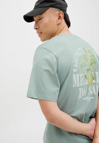 Lys grøn bomulds T-shirt med korte ærmer, der har et stort grafisk tryk på ryggen af citron grene og teksten "Originals".