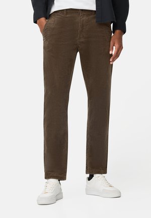 Pantalons en velours côtelé marron à coupe droite, avec des poches avant et une finition texturée, associés à des baskets blanches.