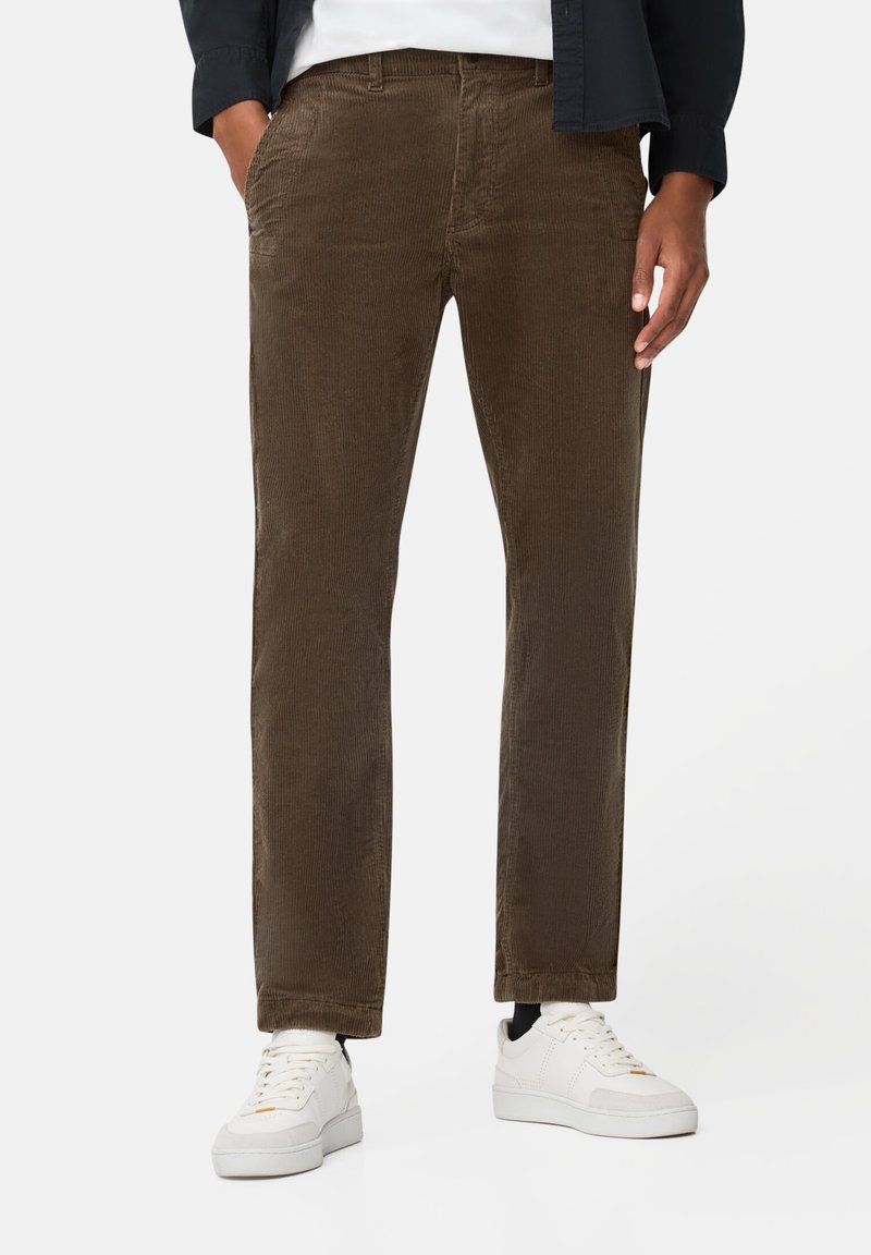 Brune corduroybukser med lige pasform, der har forlommer og en struktureret overflade, båret med hvide sneakers.