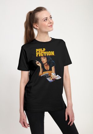 Kvinde med lys hud og hestehale iført en sort T-shirt med et Pulp Fiction-motiv af en kvinde, der holder en cigaret, en pistol og en bog.