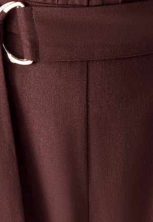 Nahaufnahme von dunkelbraunen Stoffhosen mit einem passenden Gürtel, der eine rechteckige silberne Schnalle und gestickte Nahtdetails aufweist.