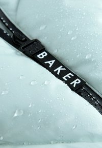Svijetloplavi vodootporan vanjski materijal s kapljicama. Crni podesivi remen sadrži riječ "BAKER" u bijelom slovu.