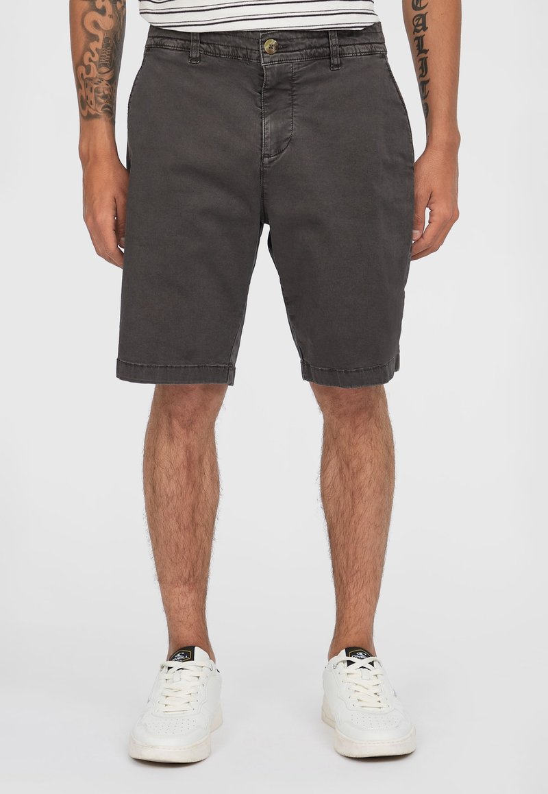Pantalones cortos de algodón gris con un corte relajado, dobladillo a la altura de la rodilla, bolsillos laterales y cierre de botón, combinados con zapatillas blancas.