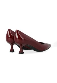 Escarpins en cuir verni bordeaux avec un bout pointu et des talons courts évasés uniques. Surface lisse avec une finition brillante, présentant un design découpé.