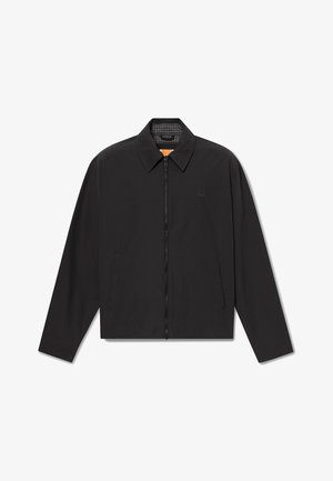 Chaqueta negra con cremallera, cuello puntiagudo, dos bolsillos delanteros y logo sutil en el pecho, mostrada extendida sobre fondo blanco.