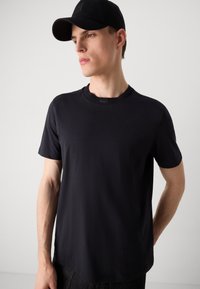 Μαύρο μπλουζάκι με κανονικό λαιμόκοψη, κοντά μανίκια και λεία υφή. Διαθέτει διακριτική επωνυμία στη λαιμόκοψη και χαλαρή εφαρμογή.