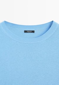 Lichtblauwe trui met ronde hals en geribbelde kraag, met een zwart label met de tekst "Massimo Dutti Made in China" aan de binnenkant van de hals.