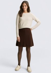 Bēšas krāsas ribots adīts īss džemperis, brūna A līnijas svārki, kopā ar melnām zeķubiksēm un krēmkrāsas slip-on apaviem; dabīga tekstūra un vienkāršs dizains.