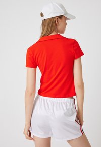 Rode polo met korte mouwen en een kraag, gecombineerd met witte sportshorts met zwarte en rode zijstrepen.