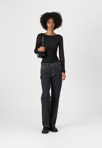 Black long-sleeve top with sheer sleeves, paired with high-waisted, wide-leg dark denim jeans, and a small black handbag. Textured appearance.