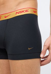 Čierne boxerky s elastickým opaskom v zlatej a červenej farbe, na ktorom je logo Nike. Hladký povrch, priliehavý strih a detail bočného šitia.