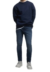 Sudadera de la marina, cuello redondo, mezcla de algodón; combinada con jeans oscuros de corte slim y zapatillas gris claro con cordones y acentos tonales.