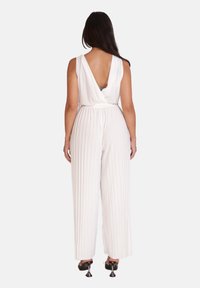 Hvid, plisseret jumpsuit med dyb V-udsnit i ryggen og vide ben. Stoffet virker blødt med en glat tekstur, suppleret af en tætsiddende talje.