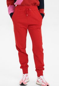 Röda sweatpants med elastisk midja och snörning, med sidofickor och mudd vid anklarna. Bärs med rosa och vita sneakers.