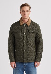 Gesteppte olivgrüne Jacke mit einem hellbraunen Kragen, ausgestattet mit zwei Brusttaschen und Druckknöpfen. Strukturierter Stoff, lässige Passform.