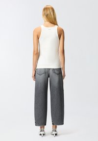 Top bianco senza maniche abbinato a jeans di denim grigi larghi. Tacchi metallici argento. Design semplice, texture liscia e senza motivi visibili.